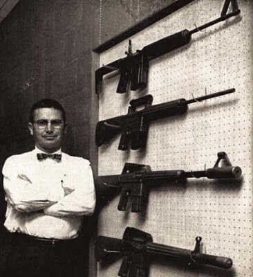 picture of eugene stoner standing next to a wall of ar15 rifles